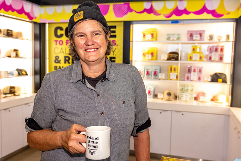 Staff member at the Wunderground coffee kiosk holding a mug, with shelves of products behind.