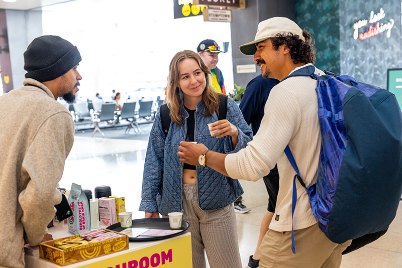 Travelers sampling products and speaking with staff at the Wunderground coffee kiosk in an airport.
