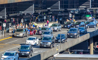 airport terminal roadway with heavy vehicle traffic and people walking along the curb.