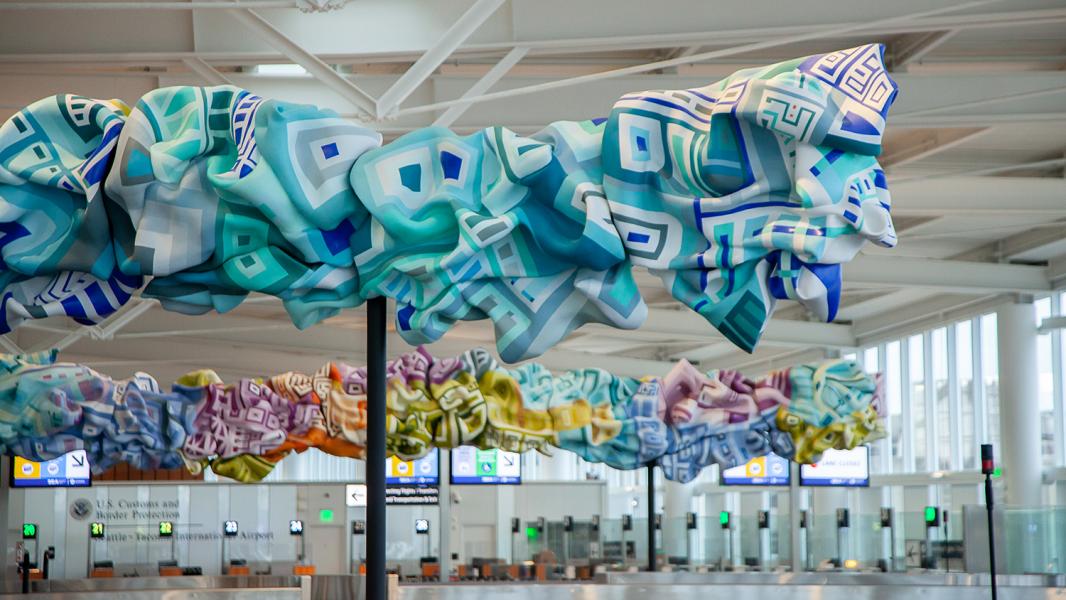 Colorful abstract sculptures hanging above airport baggage carousels.