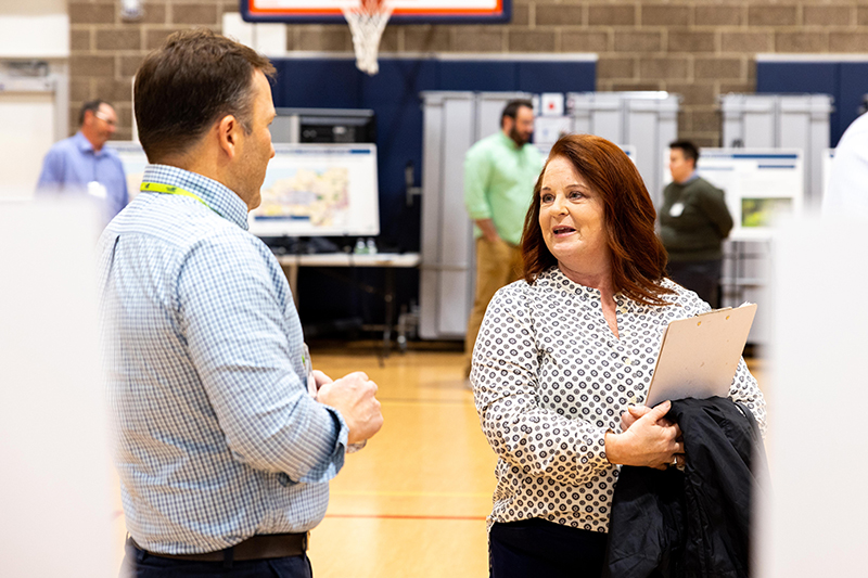People talk in a gymnasium-style room with display boards set up in the background.