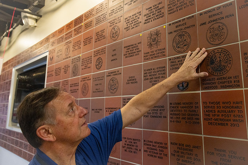 Person pointing to a memorial wall with engraved bricks honoring veterans.