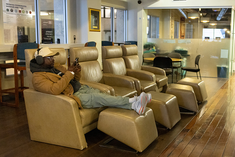 A person relaxes in a reclining chair inside the USO Northwest airport lounge, with several similar chairs, tables, and seating areas visible throughout the room.