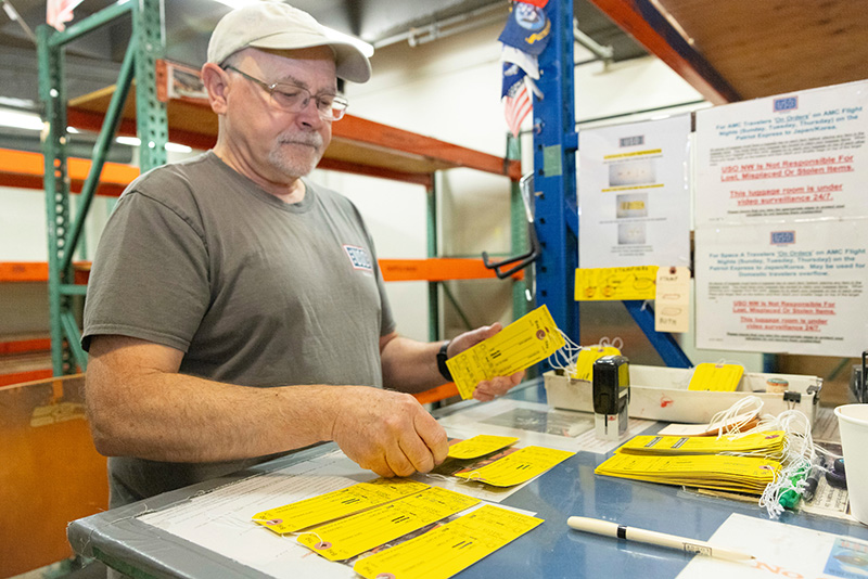 Person sorting yellow luggage tags at a workspace with shelves and posted instructions.