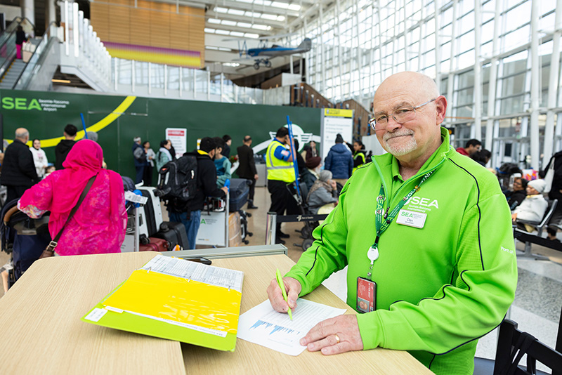 Airport staff member at a desk completing paperwork in a busy terminal area.