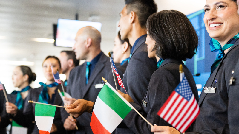 Alaska Airlines flight crew stand in a line smiling and holding Italian and United States of America flags, recognizing the new connection between the two destinations from SEA Airport