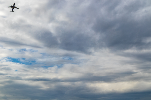 An airplane flying high in a cloudy sky with a small patch of blue visible.