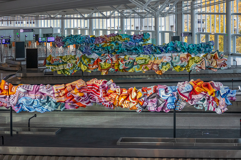 Colorful glass sculptures hang above the baggage carousels in an airport terminal.