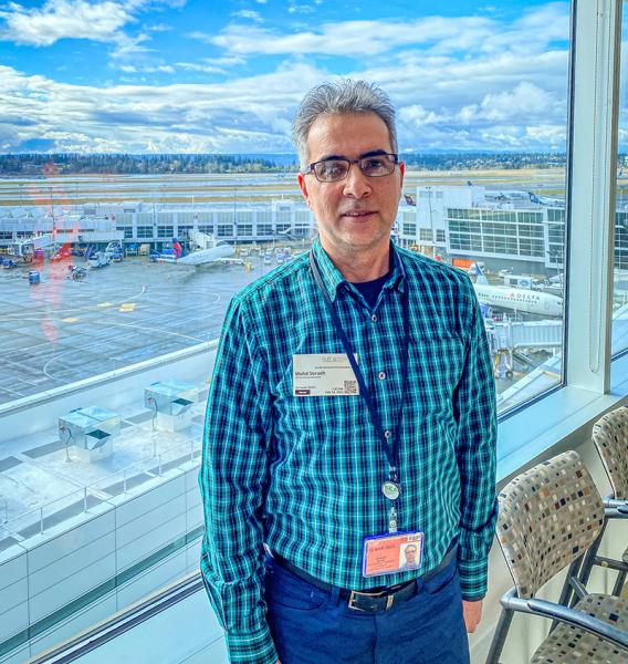 Mohd Sorush standing indoors near a window overlooking an airport terminal and runway.