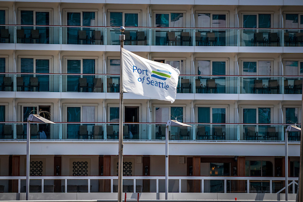 A Port of Seattle flag waving in front of the balconies of a large cruise ship.
