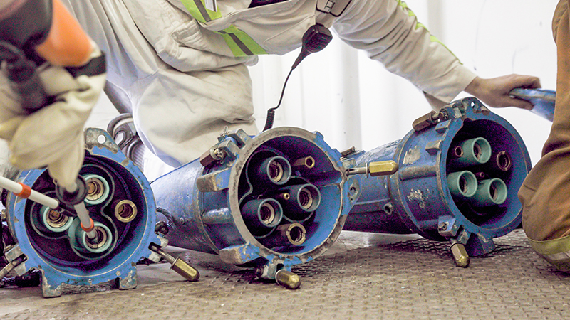 Close‑up of workers handling large blue industrial connectors with multiple openings.
