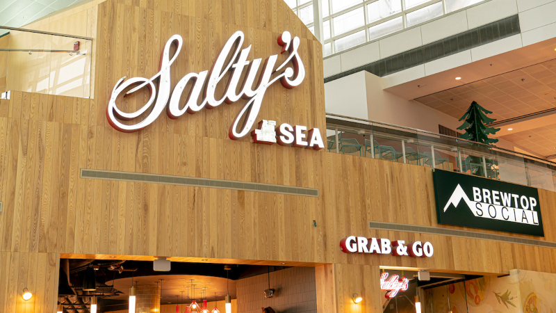 Restaurant storefronts inside an airport terminal, including signs for Salty’s Sea and Brewtop Social.