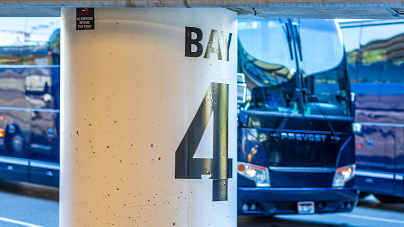 A concrete pillar labeled “Bay 4” stands in front of parked blue buses.