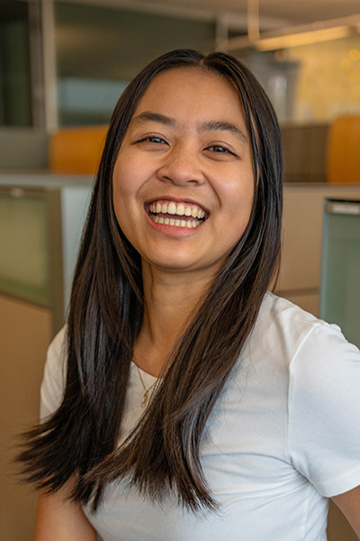 Raeanna wearing a light-colored shirt is seated in an office environment, looking toward the camera.