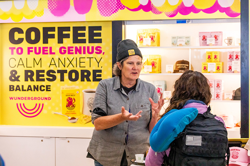 Staff member talking with a customer at the Wunderground coffee kiosk, with a large promotional sign in the background.