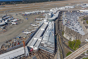 Aerial view of a large airport complex showing multiple terminals, taxiways, runways, and a multilevel parking structure.