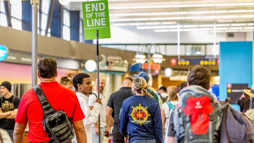 A crowded terminal area where a person holds a green sign reading “END OF THE LINE.”