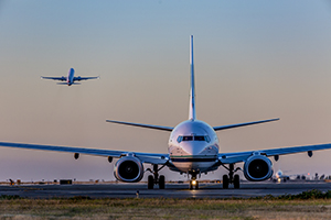 Front view of an airplane on a runway at dusk, with another airplane taking off in the background.