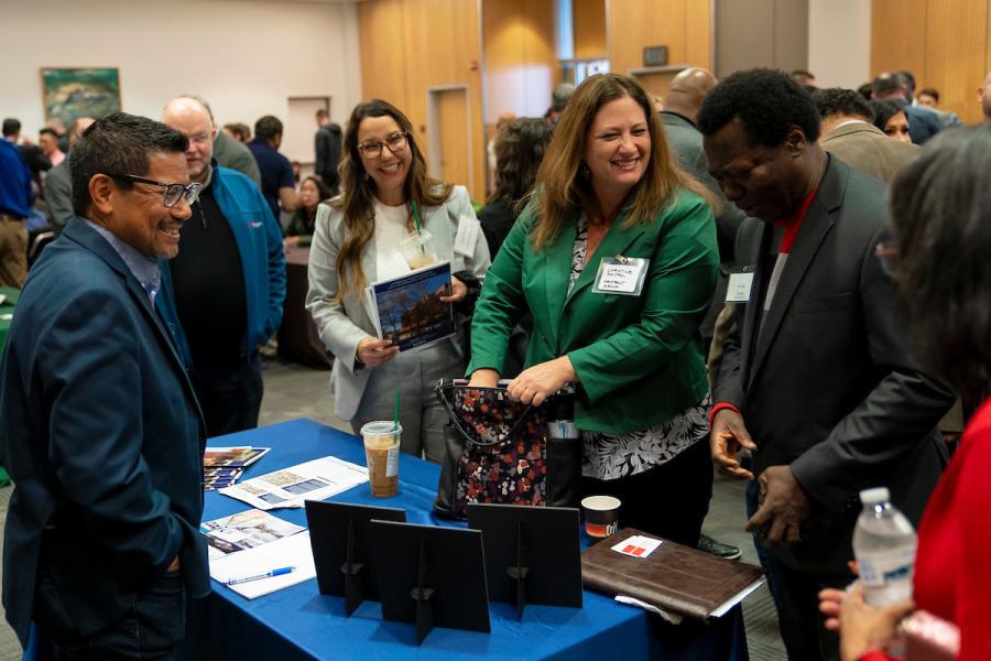 People gathered around a table at a networking event, talking and looking at materials displayed on the table.