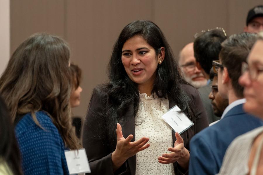 A person speaking and gesturing while conversing with others in a crowded indoor networking setting.