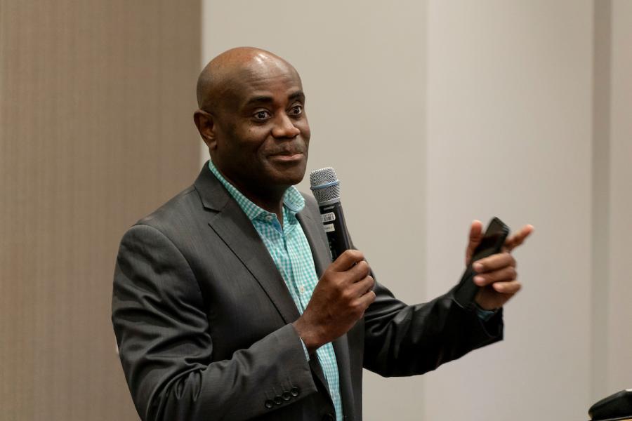 Lance Lyttle standing indoors and speaking into a handheld microphone.