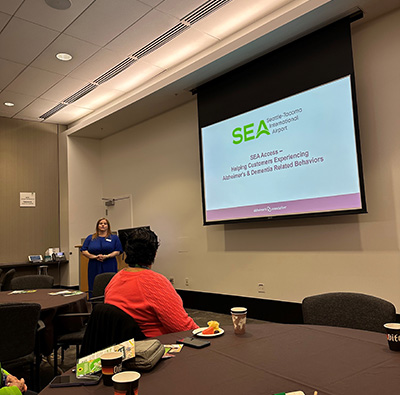 A presenter stands at the front of a conference room while attendees watch a projected SEA Airport “SEA Access” slide.