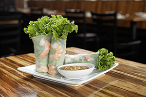 Plate of fresh shrimp spring rolls wrapped in rice paper, served with a small dish of dipping sauce.
