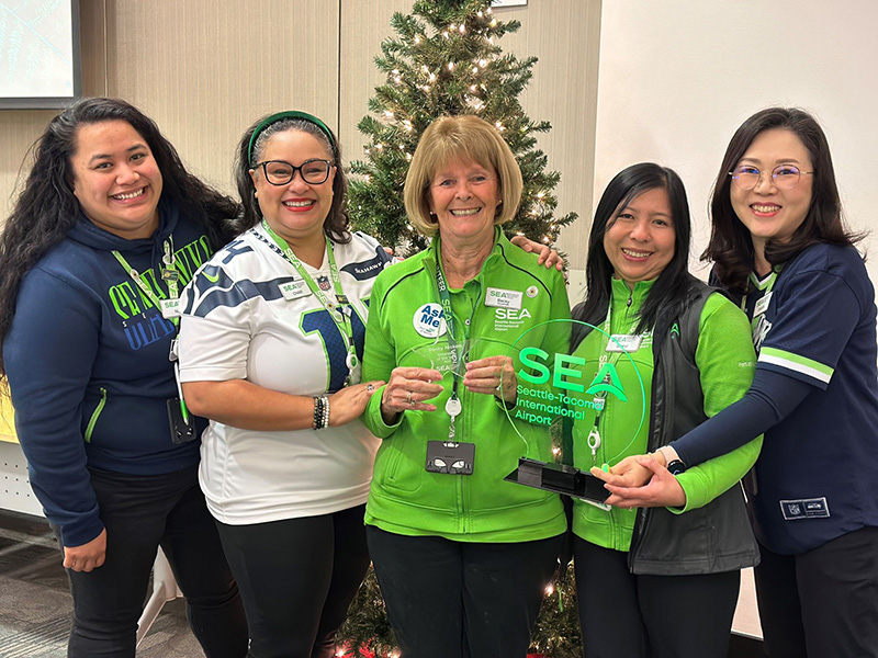 Five SEA Airport team members pose with a plaque for the 2023 Volunteer of the Year.