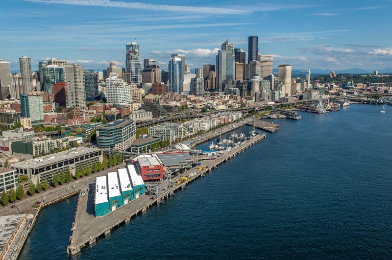 An aerial view of Seattle’s waterfront with piers, marina facilities, and the downtown skyline along Elliott Bay.