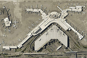 Aerial view of a large airport terminal complex with multiple concourses extending outward and numerous airplanes parked at gates.