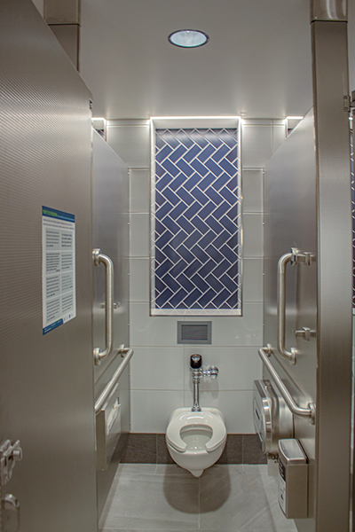 An accessible restroom stall with grab bars on both sides, a wall-mounted toilet, and a decorative tile panel on the back wall.