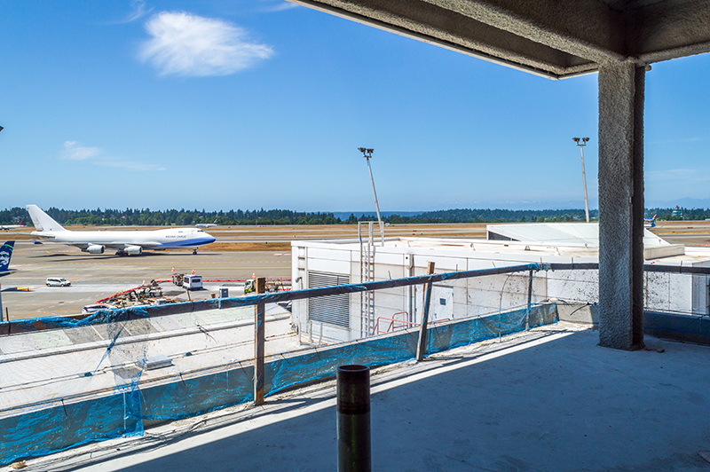 View from an unfinished public lookout showing a construction area overlooking the runway with aircraft in the background.
