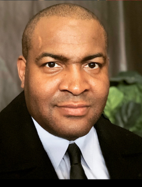 Carl Hugle in a suit and tie, looking toward the camera with a neutral expression.