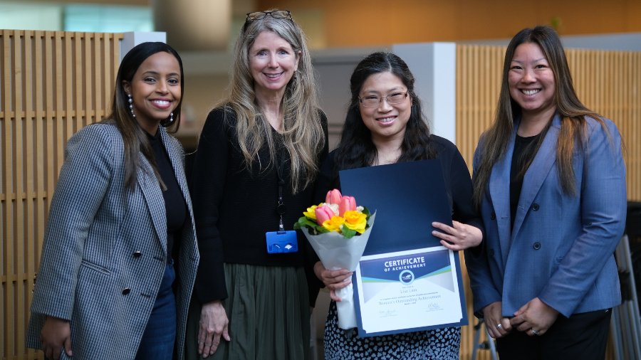 Mohamed with three female professionals, one holding a certificate of achievement and a flower bouquet.