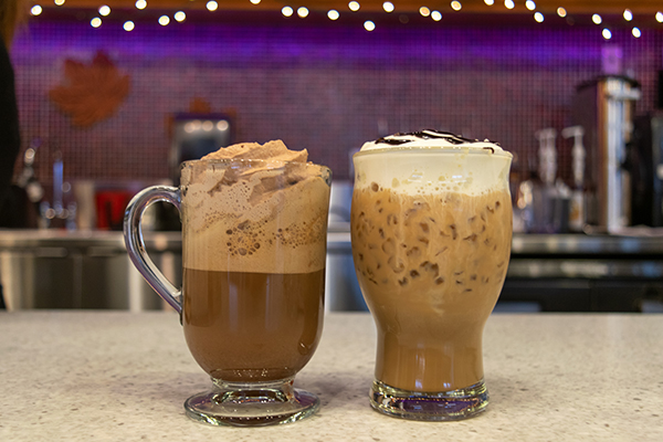 Two specialty coffee drinks on a counter, one hot and one iced, in a café setting.