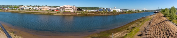A wide view of an industrial waterfront along a calm river under a clear blue sky.