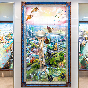 A brightly colored framed artwork depicting a surreal scene with a large brass instrument rising above a cityscape, surrounded by floating insects and abstract elements, is displayed on an indoor wall.