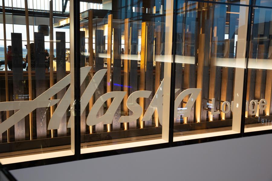 View of the Alaska Lounge logo on a glass wall with warm interior lighting behind it.