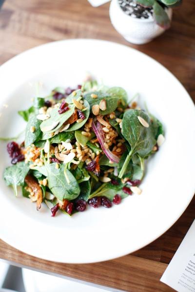 A salad with spinach, dried cranberries, and nuts served up on a white plate.