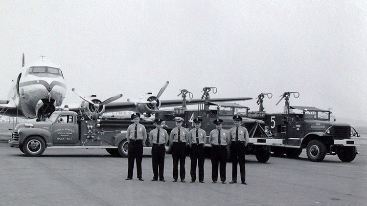 Early Port of Seattle Fire Crew stands in front of a plane.