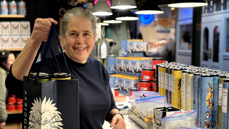 Lendy holds up a bag filled with cookie tins behind the Bite Society counter.