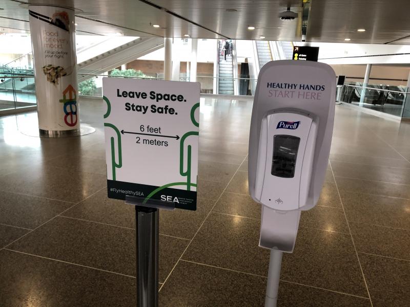 Hand sanitizer station next to a public information sign reminding passengers to stay 6 feet apart.