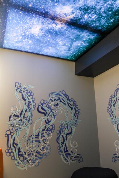 A corner of a sensory room featuring swirling blue wall art and a ceiling panel illuminated with a starry night sky pattern.