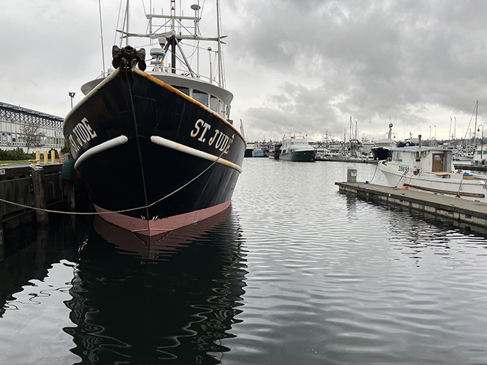 The fishing vessel St. Jude docked in a harbor on a cloudy day, with other boats moored in the background.