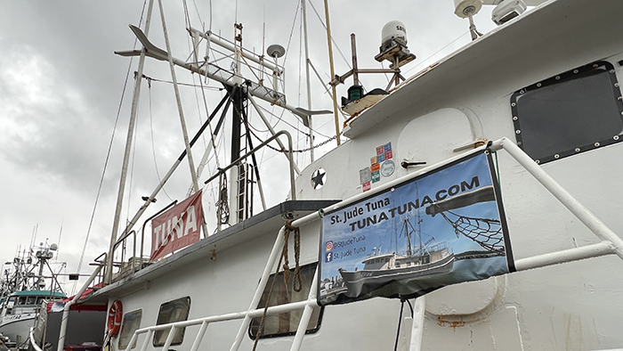 A white fishing vessel with masts and antennas docked at a marina, displaying a banner for St. Jude Tuna.