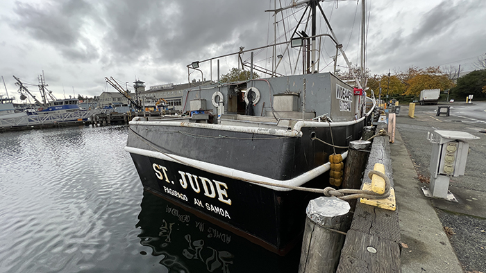 A fishing vessel named St. Jude docked beside a wooden pier on a cloudy day.