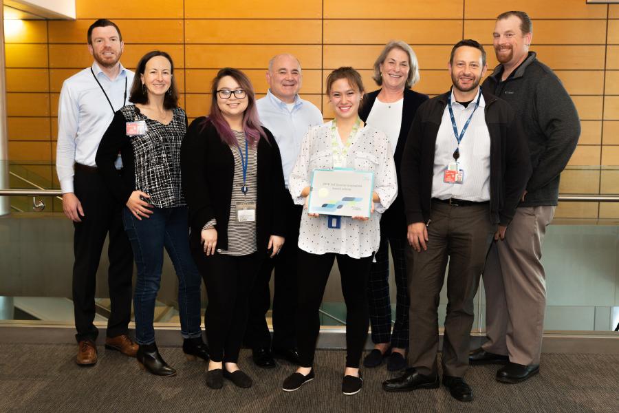 Group of people standing together in an indoor atrium, with one person holding a certificate, representing the Winning Innovative Idea Award team.