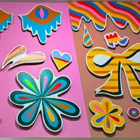 The artworks “Raindrops on Roses” and “Souvenirs” by Julie Alpert feature brightly colored, cutout shapes mounted on a pink background, including stylized flowers, hearts, raindrops, ribbons, and wavy patterns in bold striped and multicolored designs.