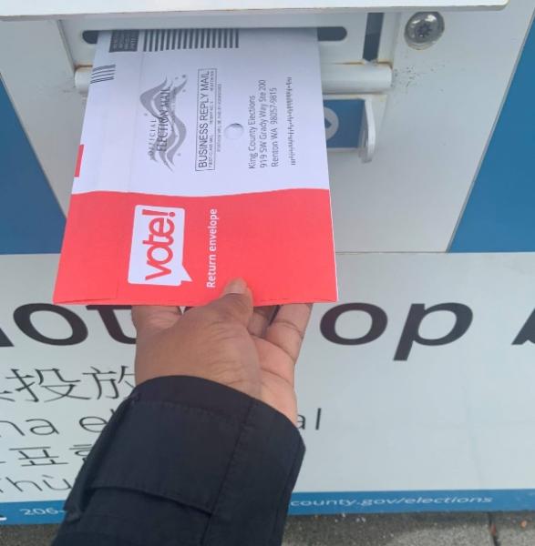 LaTonja placing a ballot return envelope into an official drop box.