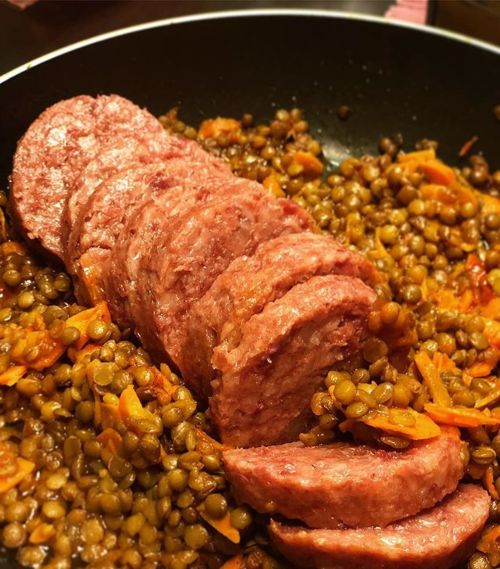 Close-up of sliced cooked sausage arranged on a bed of lentils mixed with carrots in a pan.